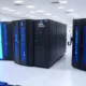 A high-tech manufacturing facility in the United States showcasing NVIDIA's DGX GH200 AI supercomputers with Hopper architecture, featuring rows of advanced systems with glowing blue lights, an American flag in the background, and researchers in white coats, symbolizing U.S. technological advancement and sovereignty.