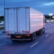 A truck on a highway at dusk with fuel price signs in the background, showcasing smart routing and optimized delivery routes to improve fuel efficiency and reduce costs in logistics.