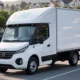 A modern white delivery truck equipped with AI and smart sensors navigating a suburban street, showcasing real-time last-mile tracking technology against a backdrop of homes and warehouses, improving delivery efficiency and customer visibility.